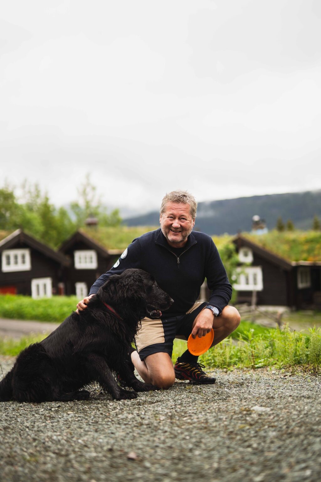 Bjarne Brøndbo med hunden sin foran tømmerhytter